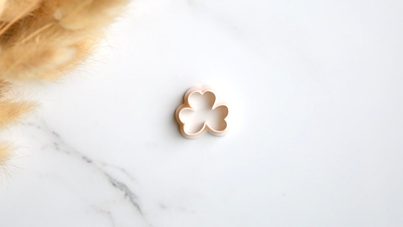 May include: A white plastic cookie cutter shaped like a three-leaf clover.