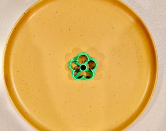 Peut inclure: Un emporte-pièce en forme de fleur en plastique vert sur une assiette beige.