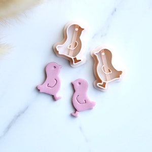 Puede incluir: Dos cortadores de galletas de pollitos de fondant rosa y dos formas de pollitos de fondant rosa.