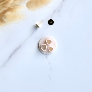 May include: A white plastic mold with three heart-shaped cutouts. The mold is on a white marble surface.