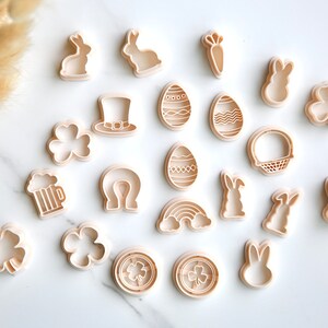 May include: A set of 19 plastic cookie cutters in various shapes, including bunnies, shamrocks, eggs, a rainbow, a horseshoe, a beer mug, a leprechaun hat, a carrot, and a basket. The cutters are white and have a light brown tint.