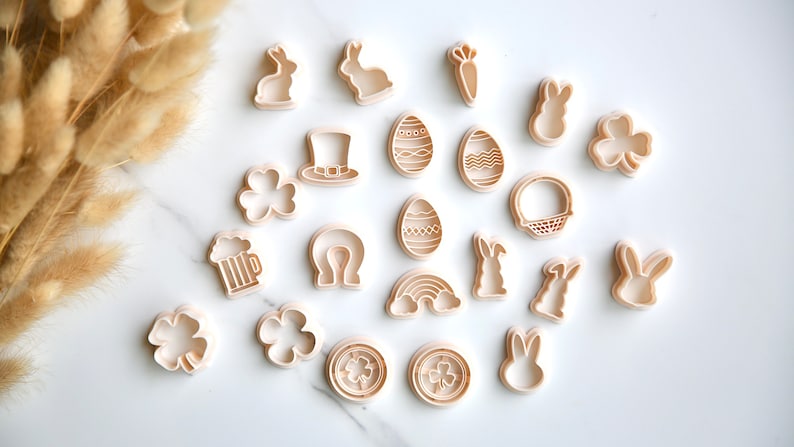 May include: A set of 19 plastic cookie cutters in various shapes, including bunnies, shamrocks, eggs, a rainbow, a horseshoe, a beer mug, a leprechaun hat, a carrot, and a basket. The cutters are white and have a light brown tint.