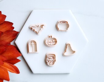 May include: A set of six white plastic Halloween cookie cutters. The cutters are shaped like a bat, a cauldron, a pumpkin, a witch's hat, a window, and Frankenstein's monster.