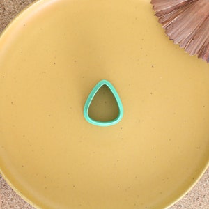 May include: A green plastic cookie cutter shaped like a teardrop on a yellow plate.