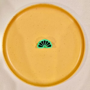 May include: A green plastic fan-shaped cookie cutter on a speckled yellow plate.