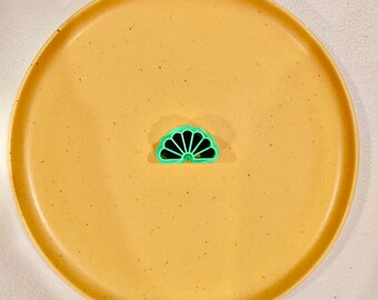 May include: A green plastic fan-shaped cookie cutter on a speckled yellow plate.