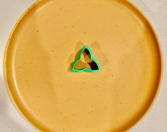 Peut inclure: Un emporte-pièce en plastique vert en forme de trèfle à trois feuilles sur une assiette beige mouchetée.