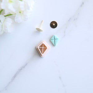 May include: A set of earring supplies including a pair of gold earring posts, a pair of earring backs, and a pair of light blue diamond-shaped earring blanks.