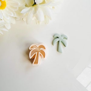 May include: Two plastic palm tree cookie cutters, one in a light green colour and one in a light pink colour.