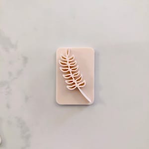 May include: A white rectangular silicone stamp with a raised design of a brown leaf.