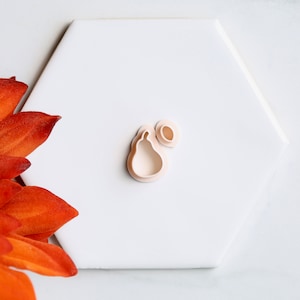 Könnte beinhalten: Zwei weiße Plastik-Ausstecher in Form einer Birne und eines Blattes.