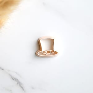 May include: A white plastic cookie cutter shaped like a leprechaun's hat. The hat has a wide brim and a tall crown with a buckle.
