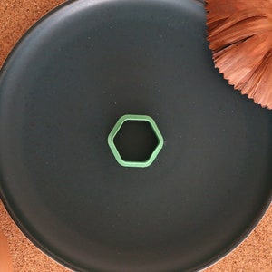 Può includere: Un tagliapasta esagonale verde su un piatto nero. Il piatto è su una superficie di sughero.