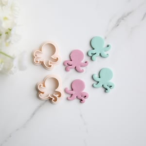 May include: Five cookie cutters and three fondant octopuses in various shades of pink and blue. The cookie cutters are white and the fondant octopuses are light pink, dark pink, and light blue.