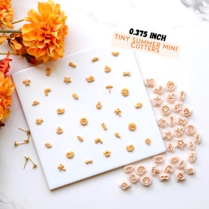 May include: A set of 0.375 inch tiny summer mini cutters. The cutters are made of plastic and are shaped like various summer-themed objects, such as seashells, starfish, and palm trees. The cutters are arranged on a white surface.