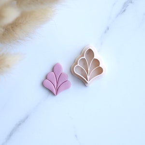 May include: A pink fondant leaf cutout with a matching plastic cookie cutter. The leaf has a stylized design with multiple rounded points.