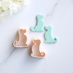 Puede incluir: Tres cortadores de galletas de plástico con forma de perros sentados. Dos son de color verde claro y uno es de color rosa claro.