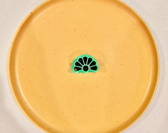 May include: A green plastic flower-shaped pasta mold on a speckled beige plate.