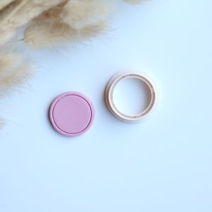 May include: A pink and white round plastic mold for making resin crafts. The mold is made of two pieces, a base and a top. The base is pink and the top is white.