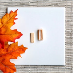 May include: Two small wooden cookie cutters, one shaped like a ruler and the other shaped like a rectangle, on a white background with a fall leaf.
