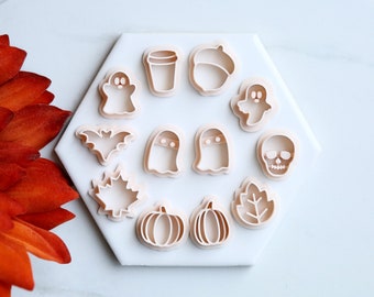 May include: A set of 12 white plastic cookie cutters featuring various Halloween and fall themes, including ghosts, pumpkins, leaves, acorns, bats, and a skull.