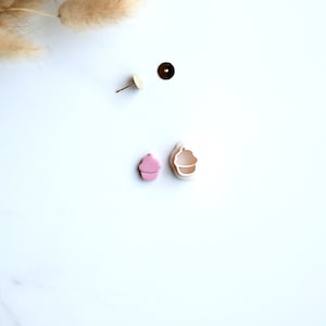 Op de afbeelding: Een paar roze cupcake-oorbellen met gouden oorbelstiften en -ruggen. De oorbellen zijn gemaakt van polymer clay en zijn gevormd als cupcakes met witte frosting en roze sprinkles.