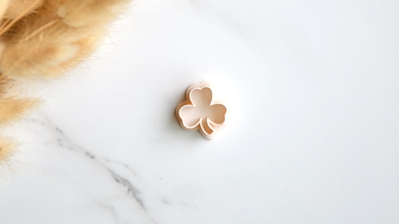 May include: A white plastic cookie cutter shaped like a four-leaf clover.