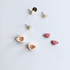 May include: A set of six earring components, including two pairs of pink and white clay cups, two gold earring posts, and two gold earring backs.