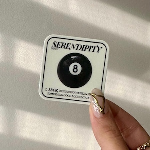 May include: White sticker with the word "Serendipity" in black text, a black and white 8-ball graphic, and the definition of the word "serendipity" in black text.