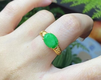 May include: A gold ring featuring a vibrant green oval-shaped gemstone. The ring has a detailed design on the band and small accent stones. The gemstone is the focal point, showcasing a rich, verdant hue.