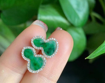 May include: A pair of green jade earrings with a diamond halo setting. The earrings are shaped like a clover leaf.