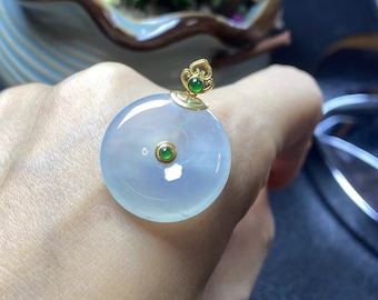 Op de afbeelding: Een ronde jade hanger met een gouden zetting en twee groene jade accenten. De hanger ligt op een hand.