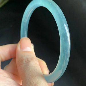 Puede incluir: Un brazalete de jade de color azul claro. El brazalete es liso y pulido.