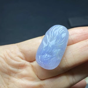 May include: A pale lavender jade pendant carved with a floral design. The pendant is oval shaped and has a smooth, polished surface.