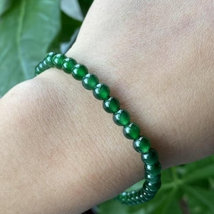 Puede incluir: Un brazalete de cuentas de jade verde con un diseño sencillo. El brazalete está hecho de pequeñas cuentas redondas que están enhebradas en un cordón delgado.