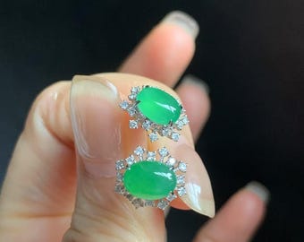 May include: A pair of jade earrings with a green oval stone set in a silver frame with small diamonds around the stone.