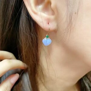 May include: A pair of dangle earrings with a light blue heart-shaped pendant and a small green gemstone accent. The earrings are made of gold.