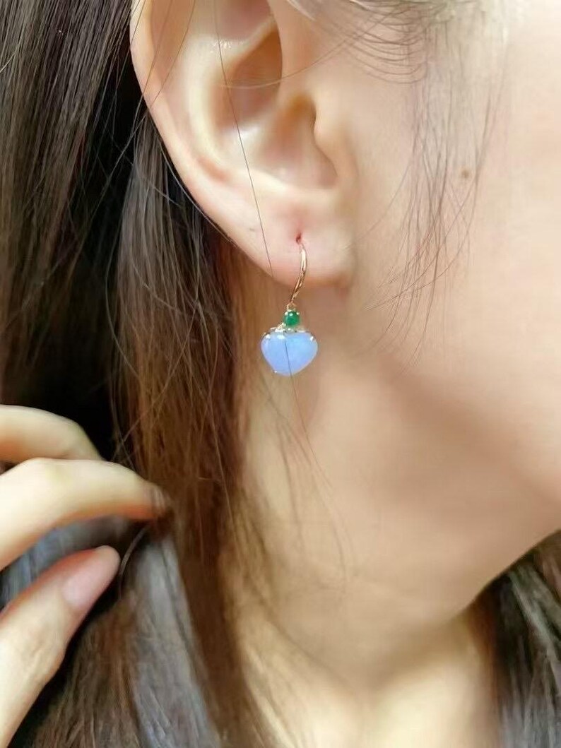 May include: A pair of dangle earrings with a light blue heart-shaped pendant and a small green gemstone accent. The earrings are made of gold.