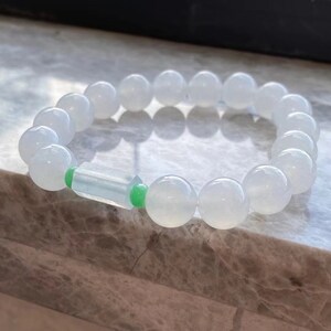 May include: A white jade bracelet with a green jade accent. The bracelet is made of round beads and has a rectangular green jade bead in the center.