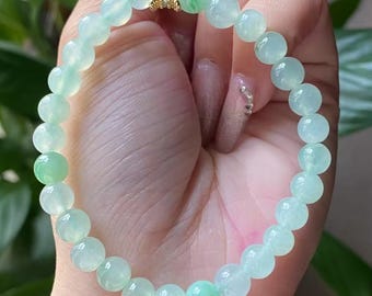 May include: A light green jade bead bracelet. The bracelet features round, translucent beads in varying shades of green, with a gold-colored spacer. The bracelet is a delicate piece of jewelry.