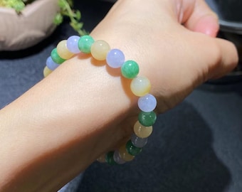 May include: A beaded bracelet featuring a variety of colors including green, yellow, and lavender. The bracelet is made of round beads and is worn on the wrist. The beads appear to be made of a polished stone.