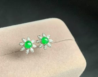 May include: A pair of silver earrings with a green jade stone in the center of each earring. The earrings are shaped like a flower with small diamonds around the jade stone.