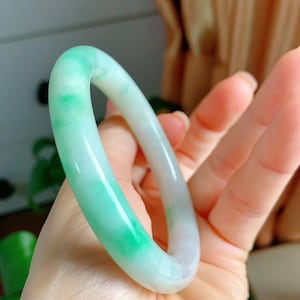 Op de afbeelding: Een groene en witte jade armband. De armband is glad en gepolijst, met een lichtgroene kleur die vervaagt naar wit.