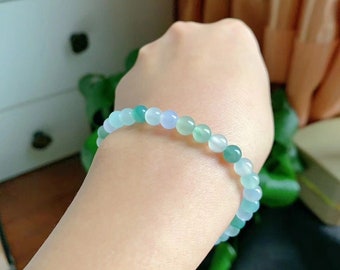 May include: A green and blue jade bead bracelet. The bracelet is made of small, round beads that are strung together on a clear elastic cord.