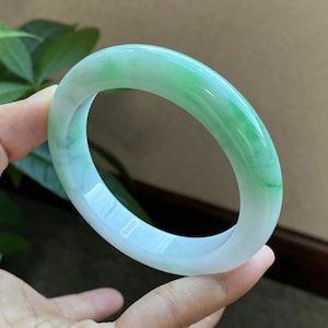 Op de afbeelding: Een jade armband met een lichtgroene kleur en witte jade. De armband is glad en gepolijst.