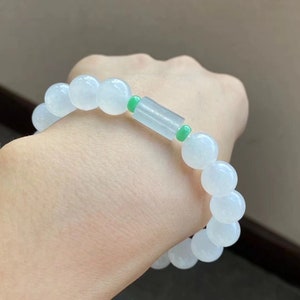 May include: A white jade bracelet with green jade accents. The bracelet is made of round beads and has a cylindrical charm in the center.