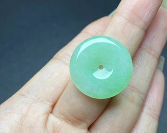 May include: A light green jade pendant in the shape of a circle with a hole in the center. The pendant is smooth and polished.