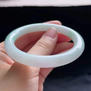 Op de afbeelding: Een lichtgroene jade&iuml;et armband. Het gladde, gepolijste oppervlak van de armband reflecteert licht en toont de doorschijnende kwaliteit. De jade&iuml;et is lichtgroen van kleur, met subtiele kleurschakeringen. Een klassiek sieraad.