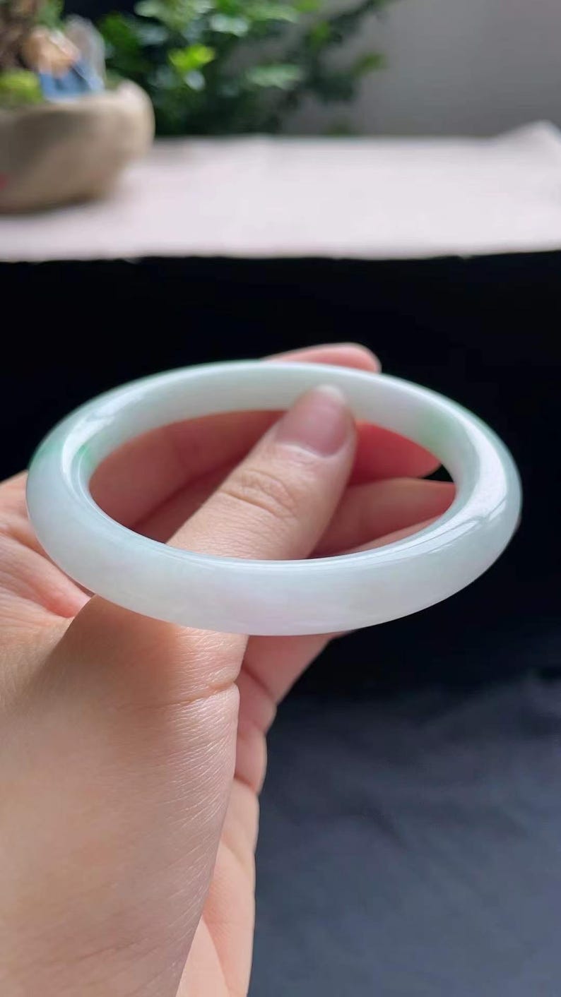 Op de afbeelding: Een lichtgroene jade&iuml;et armband. Het gladde, gepolijste oppervlak van de armband reflecteert licht en toont de doorschijnende kwaliteit. De jade&iuml;et is lichtgroen van kleur, met subtiele kleurschakeringen. Een klassiek sieraad.