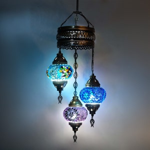 Könnte beinhalten: Ein dreilichter Kronleuchter mit einem Metallrahmen und bunten Mosaikglasschirmen. Die Schirme sind blau, lila und eine Mischung aus blau und gelb.